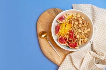 Porridge with figs, apple, nuts and napkin on wooden desk and blue backdrop. English homemade breakfast. Granola with fruits. Copy space, healthy nutrition and lifestyle