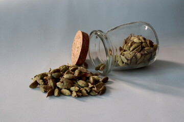 transparent glass pot, arranged on a light background, containing cardamot beans, botanical used in the preparation of gin and tonic.