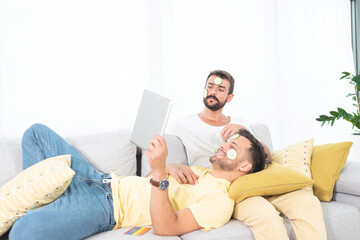 Gay couple with cucumber face mask on sofa