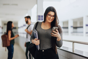 Young Brazilian student using smartphone in college. Other students in the background.