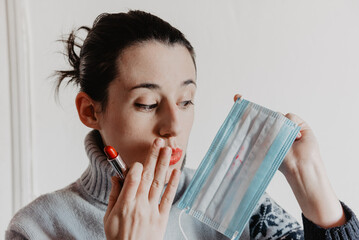 Una chica joven sujetando una mascarilla manchada por pintalabios rojo