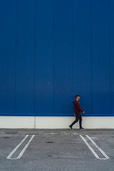 Chico joven con sudadera andando por delante de edificio azul