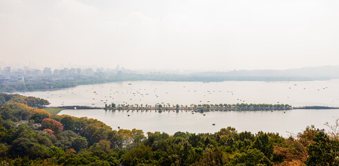 Panorama aerial view of West Lake or Xihu in early morning in autumn with Bai Causeway or Baidi, boats and cruise, Xihu District, Hangzhou, Zhejiang, China. Cityscape on background.