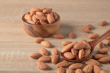 Almonds in a bowl and spoon on wooden table.