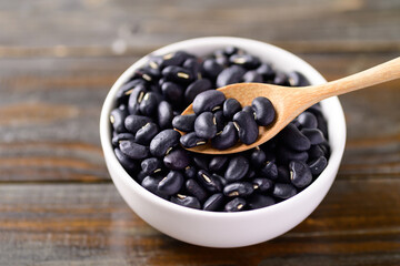 Black kidney beans in a bowl with spoon on wooden background