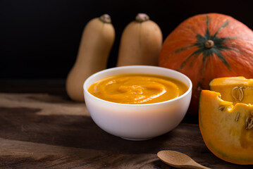 Pumpkin soup in a bowl and fresh pumpkins on wooden background