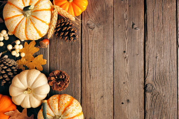 Natural fall side border of pumpkins and leaves. Top view on a rustic dark wood background with...