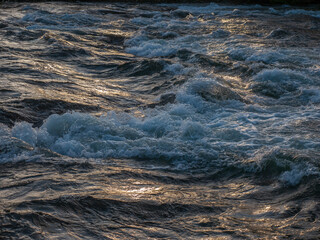 Close of shot of river water rippling and flowing golden light.