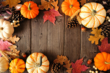 Fototapeta premium Natural fall frame of pumpkins and leaves. Above view on a rustic dark wood background with copy space.