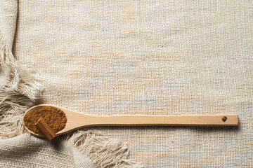 Homemade ground cinnamon and a stick in a wooden spoon on a textured cloth weaving with fringe and...