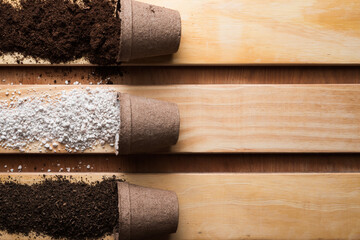 Peat moss, perlite and worm humus as substrates in peat pots for potting soil mix on pine wood boards with copy space.