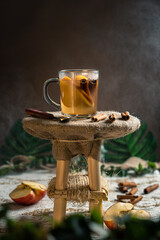 Cinnamon and apple tea on a rustic wooden stand with apples and cinnamon sticks in the table, steam in the dark background with copy space.