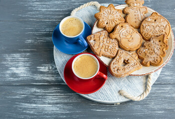 Homemade gingerbread cookies and red and blue cups with coffee on tray on grunge gray wooden background. Christmas and New Year celebration background. Close up of home baked cookies with icing