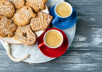 Homemade gingerbread cookies and red and blue cups with coffee on tray on grunge gray wooden background. Christmas and New Year celebration background. Close up of home baked cookies with icing.