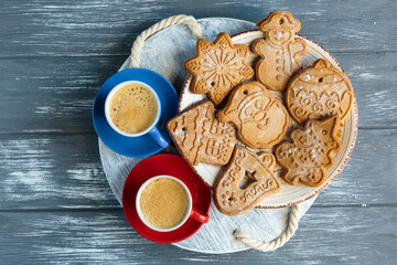 Homemade gingerbread cookies and red and blue cups with coffee on tray on grunge gray wooden background. Christmas and New Year celebration background. Close up of home baked cookies with icing.