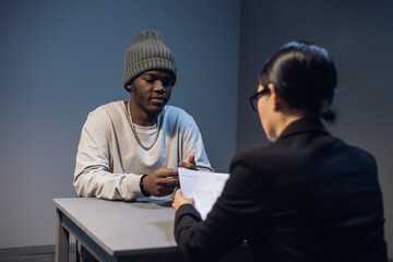 A young girl lawyer consults her client at the police station, a black guy in a cap and handcuffs