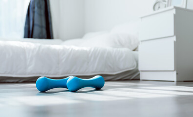 Two blue dumbbells are placed on the floor in the bedroom. Fitness at home workout.