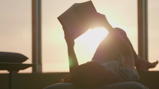 Woman relaxed reading a book outdoors lying in a balcony on the beautiful sunset background. 