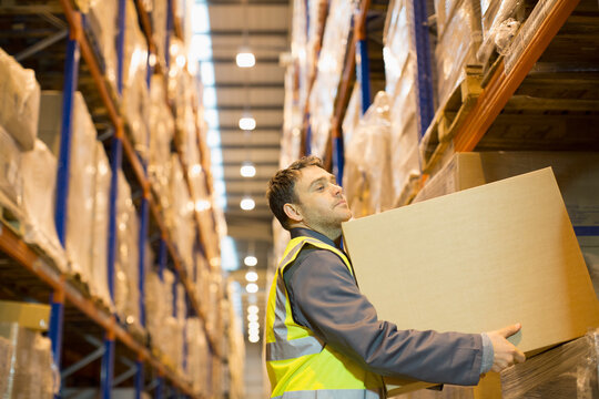Male worker lifting box from shelf in distribution warehouse