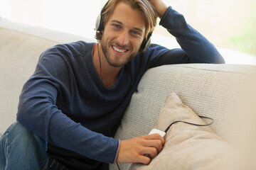 Obraz premium Portrait happy young man listening to music with headphones on sofa