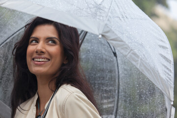 Smiling young woman with umbrella in rain © Sam Edwards/Caia Image