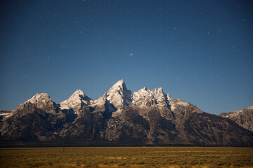 Landscape view of the Grand Teton mountain range illuminated by the full moon.