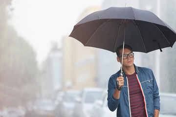 Young man with umbrella on rainy city street © Sam Edwards/Caia Image