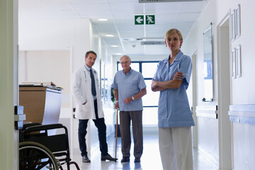 Fototapeta premium Portrait confident nurse with doctor and senior patient in hospital corridor