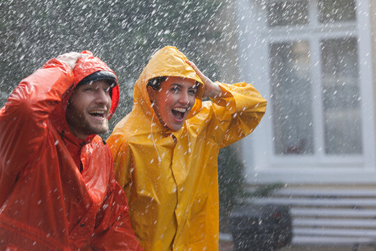 Happy couple in raincoats walking in rain