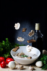 Mushroom cream soup decorated with sliced champignons and green dill and with flying ingredients. Freeze motion on black background.