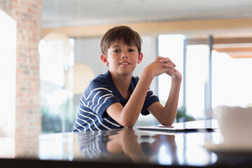 Portrait confident boy with digital tablet at kitchen counter © Martin Barraud/Caia Image