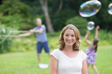 Fototapeta premium Portrait happy woman playing with bubbles with family in backyard
