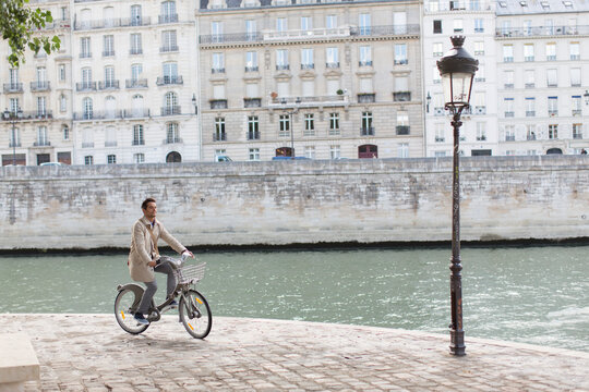 Businessman riding rented bicycle along Seine River, Paris, France