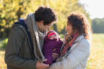 Fototapeta premium Happy young couple holding baby daughter in sunny park