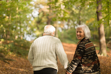 Fototapeta premium Portrait smiling senior couple holding hands and walking in autumn park