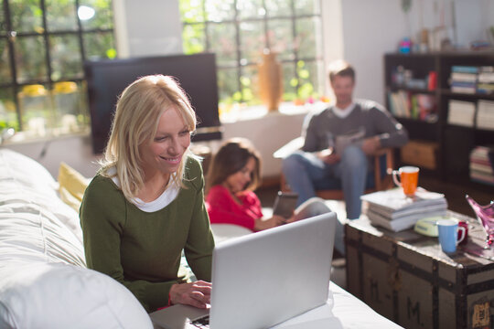 Young woman using laptop on sofa in living room with roommates