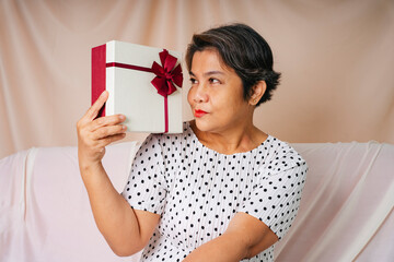 Cool old elderly senior woman in white polka dot dress with birthday gift box.