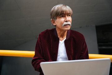 Portrait of old senior engineer working outdoors with laptop.