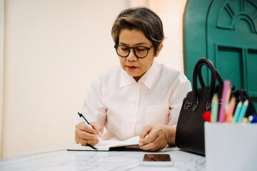 Fototapeta na wymiar Elderly senior old woman wear eyeglasses writing diary on a book.