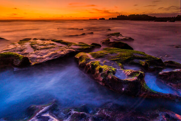 Mangening Beach at Canggu Bali with long exposure technique for slow speed water. Big wave with rock with green moss layer on sunset at the beach. 