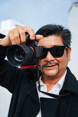 Old elderly senior photographer wearing sunglasses holding mirrorless camera.