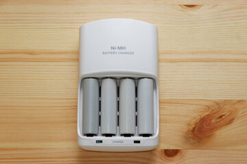 Rechargeable AA battery in a white charger on wooden background.Top view.