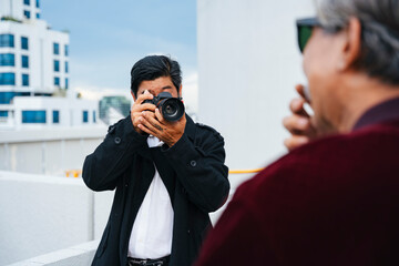 Adult photographer taking photo of cool old man in city.