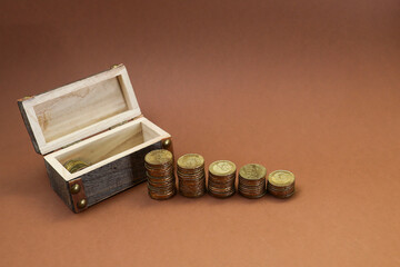 Stack of coins with a wood chest on brown background