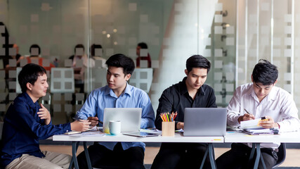 Young asian male office workers meeting and planning work together at their desk.