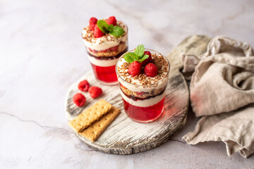Dessert in a glass cup, with Jello covered in yogurt and topped with fresh raspberries. Mini dessert on light concrete background. Fruit parfait with jello and jelly. 