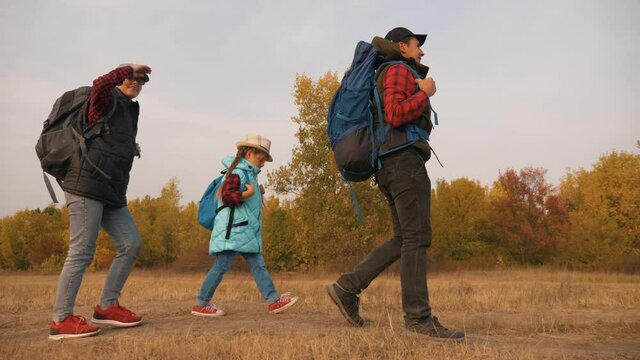 Happy family of tourists. People with backpacks go to the field in the open area with a hike. Weekend hobby in the woods. Family vacation tourism with children on a summer hike.