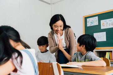 Young Asian teacher giving boy high five in school, success, achievement, happiness. Asia school boy with young woman in class. - 383200771