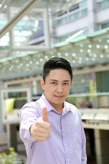 Young south east Asian man business office outdoor stand look at camera thumbs