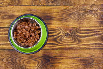 Canned food for cats or dogs in green metal bowl on wooden floor. Top view